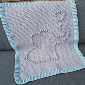 May include: A grey crochet baby blanket with a blue border. The blanket features a textured elephant design with a heart-shaped balloon. The blanket is made of soft yarn, ideal for a baby. The blanket is approximately 100cm x 100cm.