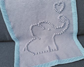 May include: A handmade crochet baby blanket in gray with a blue border. The blanket features a textured elephant design with a heart-shaped balloon. The blanket is made of soft yarn and is perfect for a baby.
