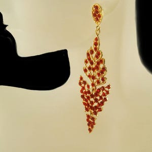 Op de afbeelding: Een paar gouden oorbellen met rode kristallen accenten. De oorbellen zijn traanvormig met een cascade-ontwerp.