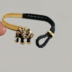 May include: A gold and black bracelet with an elephant charm. The elephant is black with gold accents and rhinestones.
