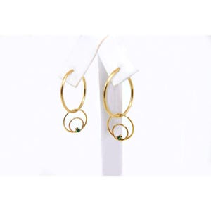 May include: Gold hoop earrings with a smaller circle dangling from each hoop. Each smaller circle has a small green gemstone in the center.