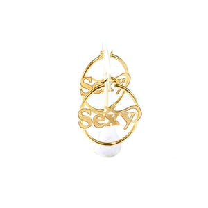 May include: Gold-coloured hoop earrings with the word "Sexy" in a cursive font. The earrings are displayed against a white background. The word "Sexy" is attached to the bottom of the hoop.