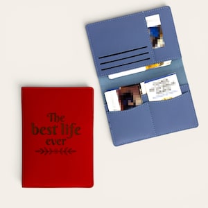 May include: A red passport holder with the text "The best life ever" and a floral graphic, alongside an open blue passport holder featuring multiple interior card slots and pockets containing various identification cards and documents.