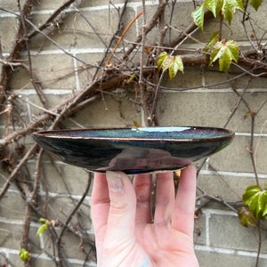 May include: A dark blue ceramic dish with a slight iridescent sheen. The dish is shallow and has a rounded rim.