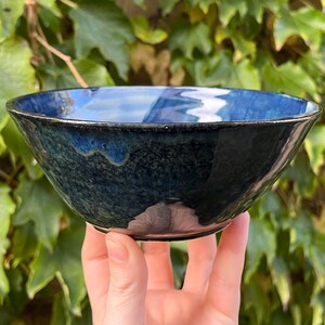 May include: A deep blue ceramic bowl with a speckled glaze. The bowl is slightly wider at the top than the bottom and has a rounded shape.