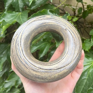 May include: A ceramic ring with a textured, brown and gray glaze. The ring has a large, circular opening in the center.