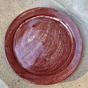 May include: A red ceramic plate with a white speckled glaze. The plate has a raised rim and a slightly textured surface.