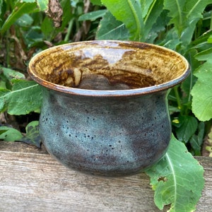 May include: A small, ceramic bowl with a teal glaze and brown speckles. The bowl has a wide rim with a brown glaze.