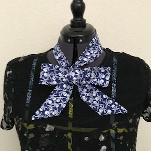 Peut inclure: Un chemisier noir avec un nœud papillon à motif de crânes et d'os croisés blanc et bleu.