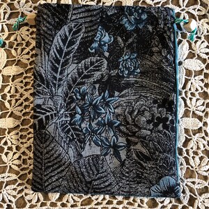 Pode incluir: Uma pequena bolsa de cordão preta e azul com um padrão floral. A bolsa é feita de tecido e tem um fecho de correr.