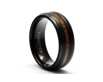 Puede incluir: Anillo de tungsteno negro con una incrustación de madera marrón. El anillo está grabado con la palabra "TUNGSTEN".