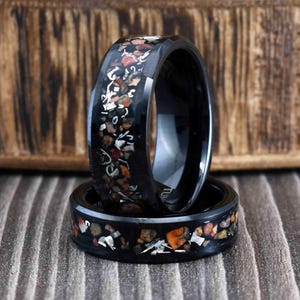 May include: Two black ceramic rings with a pattern of small, colorful stones embedded in the band. The rings are stacked on top of each other.