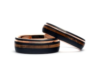 May include: Two black tungsten carbide rings with rose gold inlays and wood accents. The rings are stacked on top of each other.