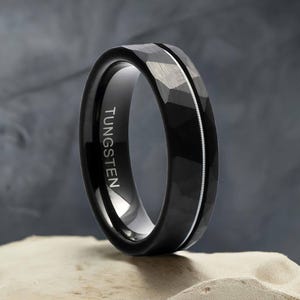 May include: A black tungsten ring with a silver line down the center. The ring has a hammered finish and the word "TUNGSTEN" is engraved on the inside of the band.