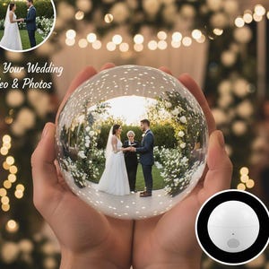 Può includere: Una sfera di vetro trasparente che riflette una cerimonia nuziale, tenuta in mani a coppa. La sfera ha un piccolo altoparlante bianco e il testo "Plays Your Wedding Video & Photos" e "Plays Video With Sound". Lo sfondo presenta luci a corda e composizioni floreali.