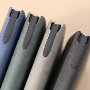 May include: Four slim, rectangular cases in blue, green, gray, and black with a black elastic band closure.
