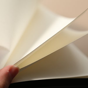 May include: A close-up of a blank, white notebook with pages turned open. The pages are smooth and have a slight sheen. The notebook is bound in black.