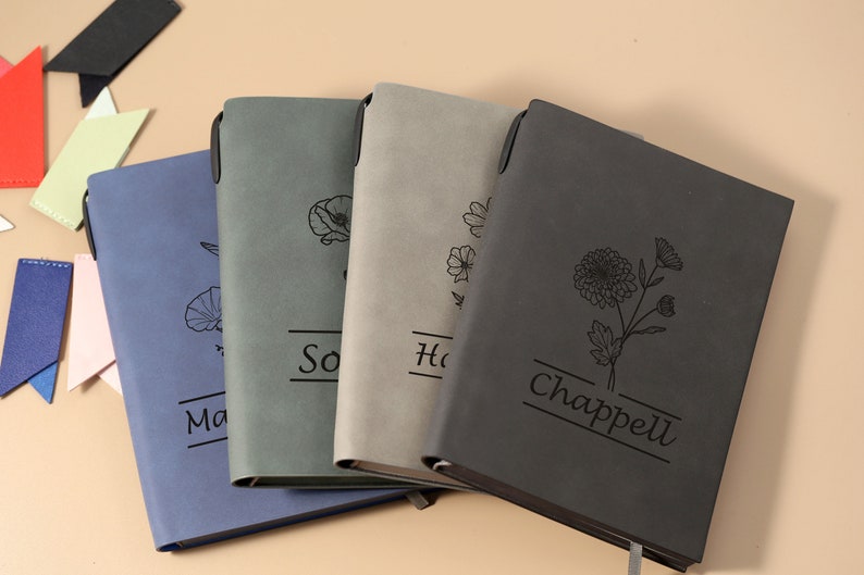 May include: Four gray, blue, and black journals with floral designs and personalized names. The names are "Sophia", "Hannah", and "Chappell".
