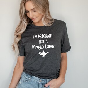 May include: A dark gray t-shirt with the text "I'm Pregnant Not A Magic Lamp" in white lettering. A white silhouette of a magic lamp is below the text.