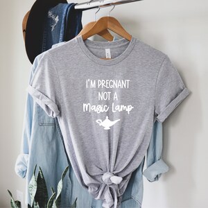 May include: A grey t-shirt with the text "I'm pregnant not a magic lamp" in white lettering. A white silhouette of a magic lamp is below the text.