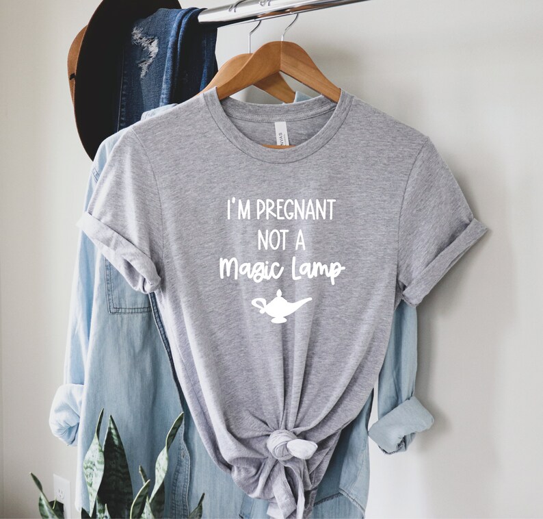 May include: A grey t-shirt with the text "I'm pregnant not a magic lamp" in white lettering. A white silhouette of a magic lamp is below the text.