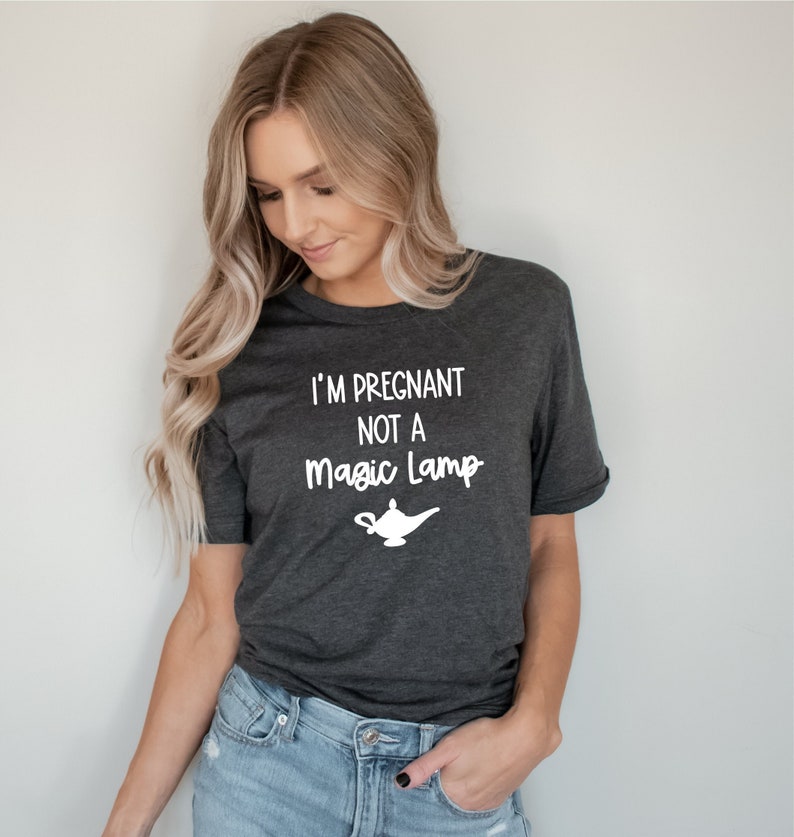 May include: A dark gray t-shirt with the text "I'm Pregnant Not A Magic Lamp" in white lettering. A white silhouette of a magic lamp is below the text.