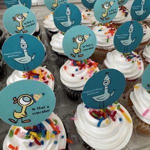 May include: Cupcakes with white frosting and colorful sprinkles, topped with blue circular toppers featuring a cartoon pigeon and the text "Is that a cupcake?" and "Happy Birthday Beckham."