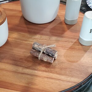 Può includere: Un vassoio di legno con un bordo in metallo nero, che presenta tre piccoli fasci di ramoscelli legati insieme con uno spago. Ci sono anche due saliere e pepiere in ceramica bianca sul vassoio.