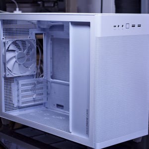 以下が含まれることがあります： メッシュのフロントパネルと内部にファンが見える白いコンピューターケース。ケースの側面には「ASUS PRIME CASE」と書かれた黒いラベルが付いています。