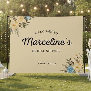 May include: A beige bridal shower sign with floral accents and the text "Welcome to Marceline's Bridal Shower, 12 March 2026." The sign is set up outdoors with decorative lights and chairs.