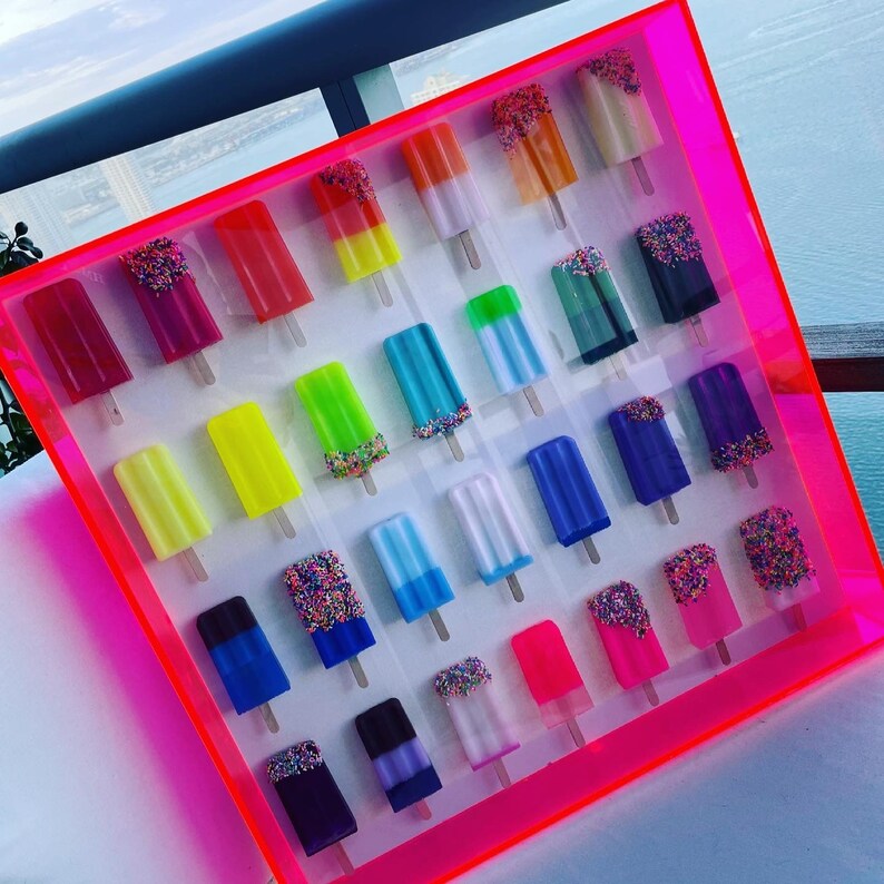 Puede incluir: Un marco rosa lleno de decoraciones coloridas con forma de paleta de helado. Las paletas de helado est&aacute;n dispuestas en filas y columnas, cada paleta tiene un color y un dise&ntilde;o diferente.