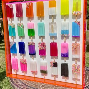 Puede incluir: Una pieza de arte de pared enmarcada que presenta 25 paletas de colores con chispas. Las paletas est&aacute;n dispuestas en cinco filas de cinco, con cada fila presentando una combinaci&oacute;n de colores diferente. El marco es de color naranja brillante.