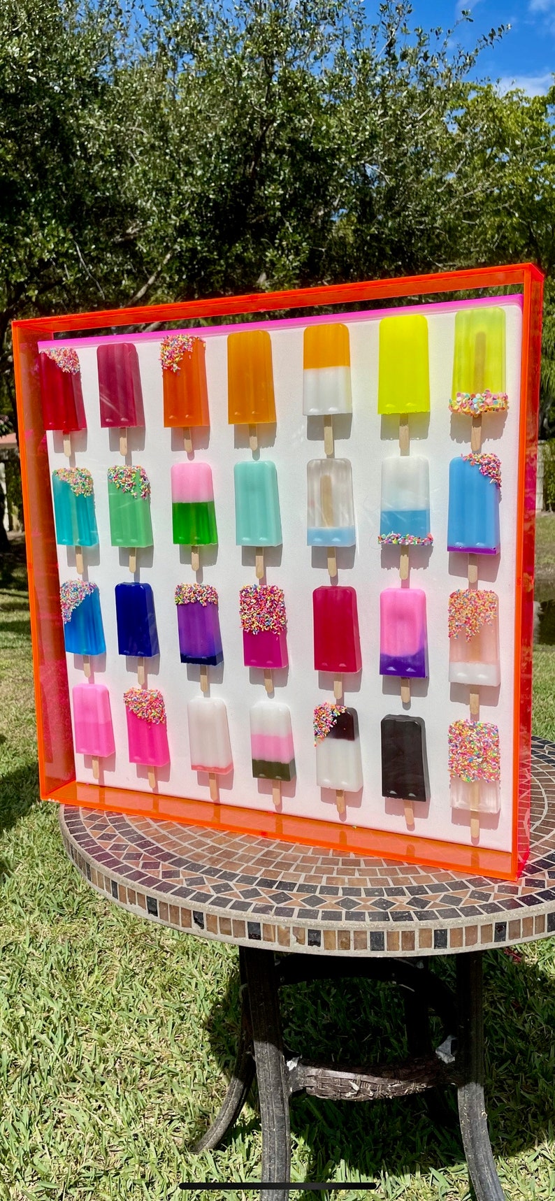 Puede incluir: Una pieza de arte de pared enmarcada que presenta 25 paletas de colores con chispas. Las paletas est&aacute;n dispuestas en cinco filas de cinco, con cada fila presentando una combinaci&oacute;n de colores diferente. El marco es de color naranja brillante.