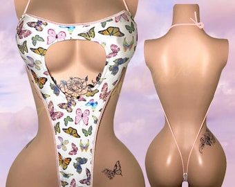 Può includere: Costume da bagno intero bianco con stampa a farfalle multicolore. Il costume ha un collo all'americana e uno scollo a forma di cuore sul petto. I bordi sono rosa.