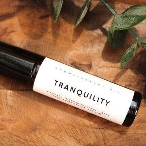 May include: A black roller bottle with a white label that reads "AROMATHERAPY OIL TRANQUILITY A PEACEFUL BLEND OF PATCHOULI, YLANG YLANG, SWEET ORANGE AND LIME"