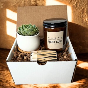 May include: A gift box containing a small succulent in a white pot, a candle with a black lid, and a matchbox. The candle label reads "HAPPY FATHER'S DAY TO THE BEST DAD EVER!" The box is filled with brown paper shreds.