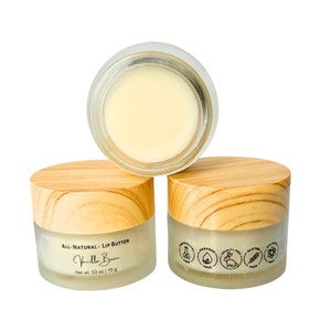 Puede incluir: Tres frascos de vidrio con tapas de madera llenos de b&aacute;lsamo labial blanco. El frasco en el frente tiene una etiqueta que dice "All-Natural - Lip Butter Vanilla Bean Net wt. .53 oz / 15 g". El frasco en la parte posterior tiene una etiqueta con &iacute;conos para libre de parabenos, libre de fragancias, libre de crueldad, libre de gluten y vegano.