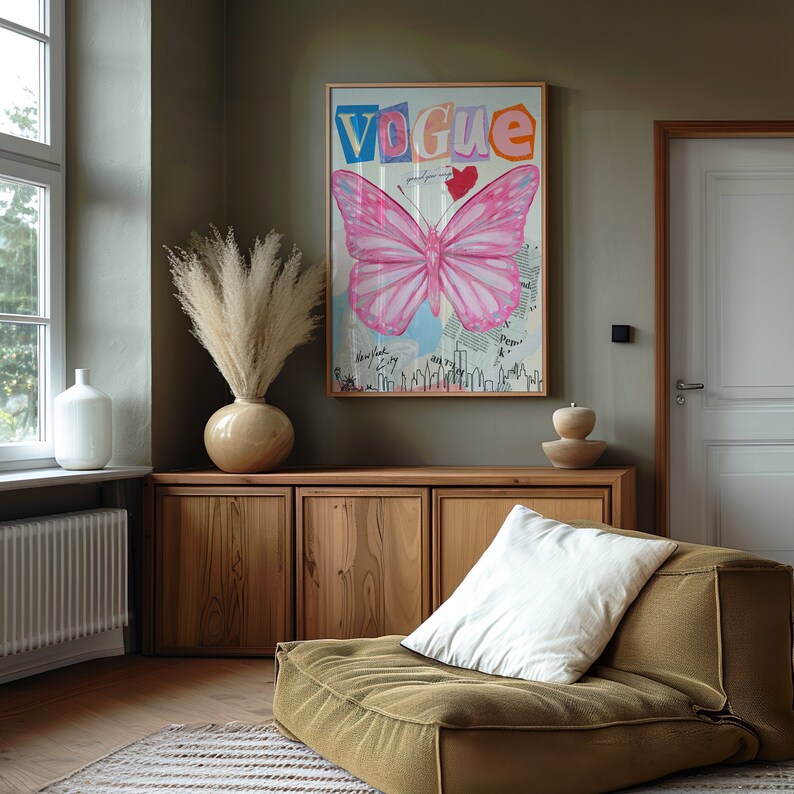 May include: A wooden cabinet with three doors, a vase with dried pampas grass, a pink butterfly illustration with the word "Vogue" in colourful letters, and a brown ottoman with a white cushion.