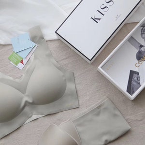 May include: A light grey seamless bra and matching underwear set with the word "Kiss" printed on the underwear. The bra has a V-neck and the underwear has a low rise.