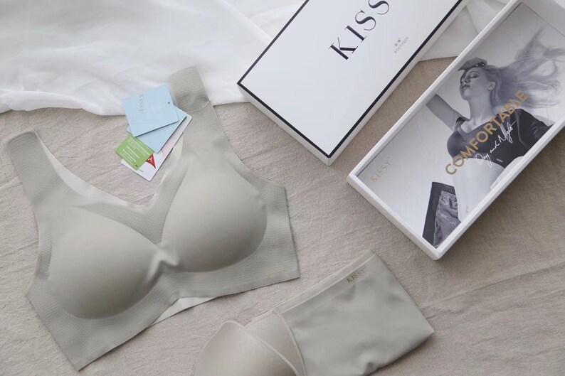 May include: A light grey seamless bra and matching underwear set with the word "Kiss" printed on the underwear. The bra has a V-neck and the underwear has a low rise.