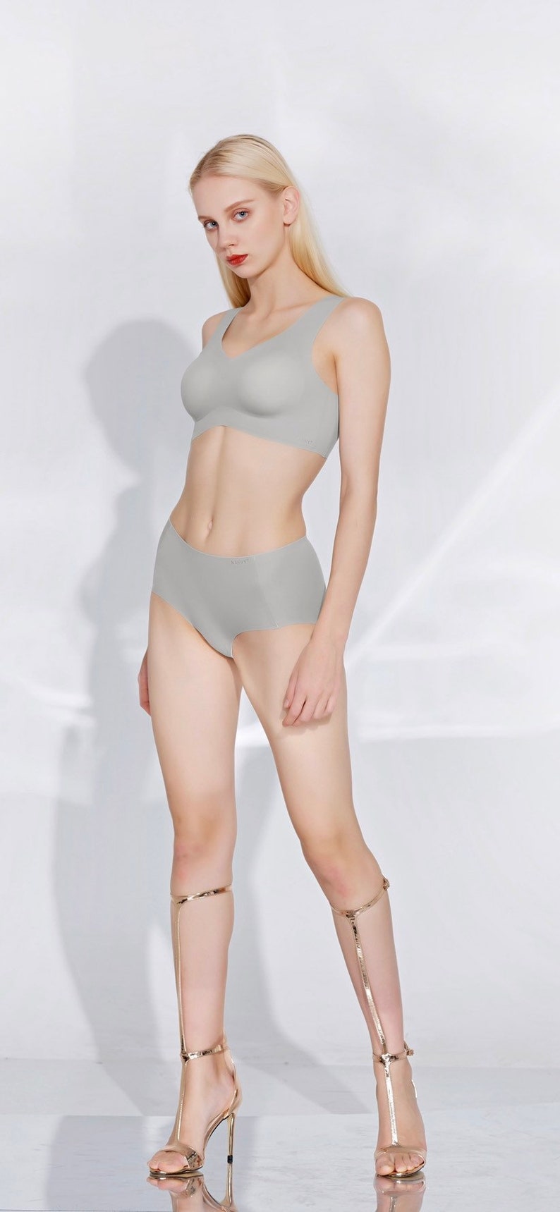 May include: A woman is wearing a light grey seamless bra and matching underwear. She is wearing gold high-heeled sandals.