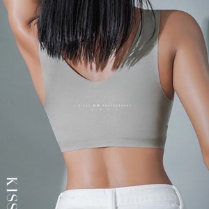 May include: A woman wearing a light grey seamless tank top with the text "KISSY PHOTOGRAPHY" printed on the back. She is wearing white jeans.