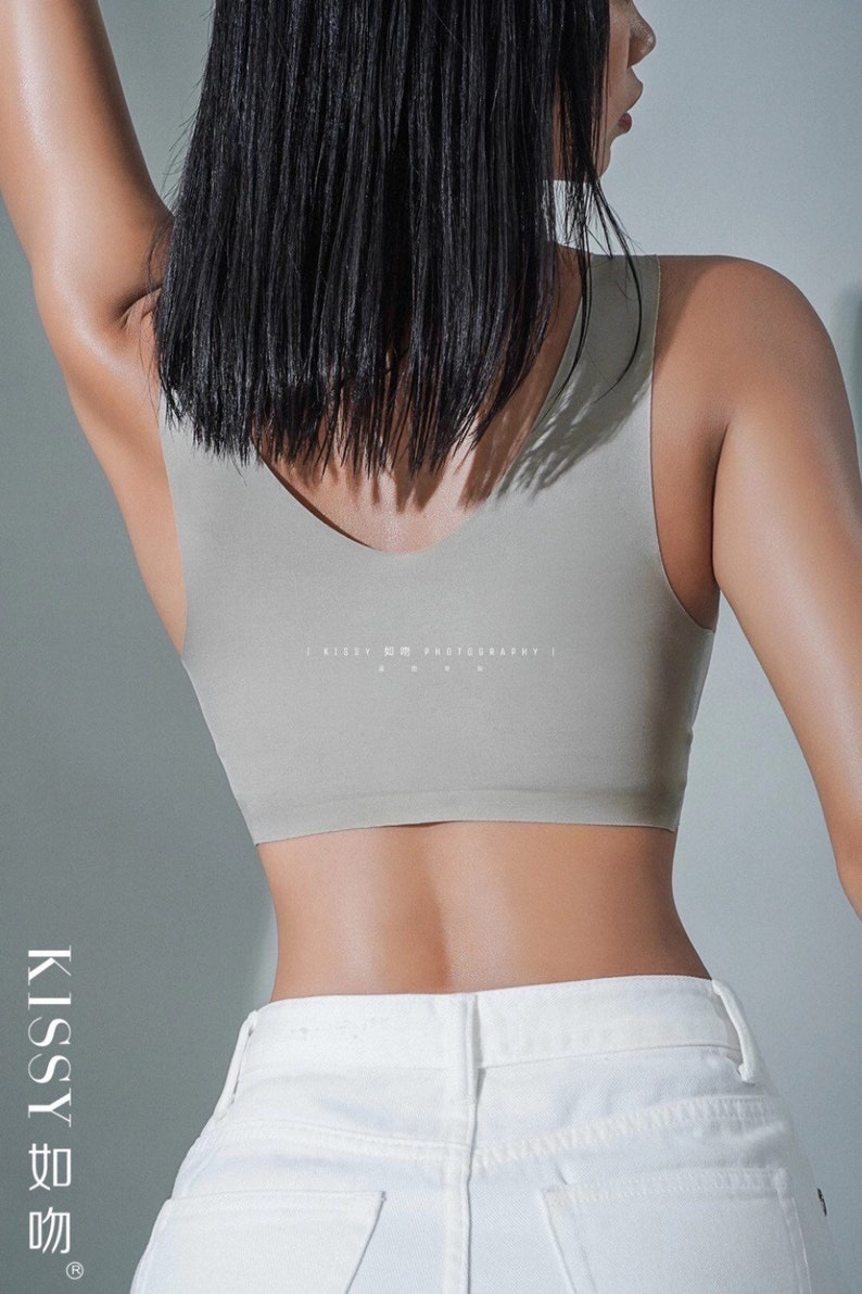May include: A woman wearing a light grey seamless tank top with the text "KISSY PHOTOGRAPHY" printed on the back. She is wearing white jeans.