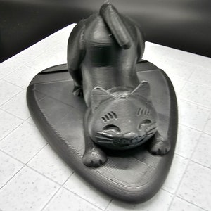 May include: A black 3D printed cat figurine with a playful expression, sitting on a black heart-shaped base.