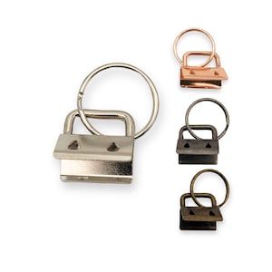 Könnte beinhalten: Drei silberne, schwarze und bronzene Schlüsselringe mit einem Drehverschluss. Jeder Ring hat ein kleines, rechteckiges Metallstück mit zwei Löchern.