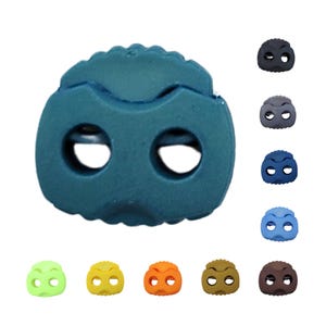 Könnte beinhalten: Eine Auswahl an farbenfrohen Kordelstoppern aus Gummi in verschiedenen Farbtönen wie Teal, Schwarz, Grau, Blau und Braun. Die Kordelstopper haben zwei Ösen und eine strukturierte Oberseite, geeignet zum Einstellen von Kordeln an Kleidung oder Ausrüstung.