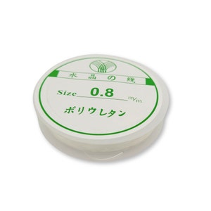 May include: A white plastic container with a clear lid containing white string. The label on the container is green and white and reads "Size 0.8 mm" and "ポリウレタン" in Japanese.