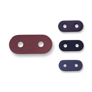 Pode incluir: Três conectores de correia de couro com dois furos cada. Os conectores são de cores diferentes: bordô, azul escuro e azul claro.