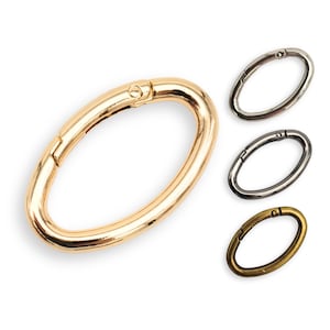 May include: Three oval-shaped metal clasps in gold, silver, and bronze. The clasps are open and have a spring-loaded mechanism.