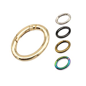 May include: Five oval-shaped metal key rings in different colours: gold, silver, black, bronze, and iridescent. The key rings are open and have a spring-loaded mechanism.